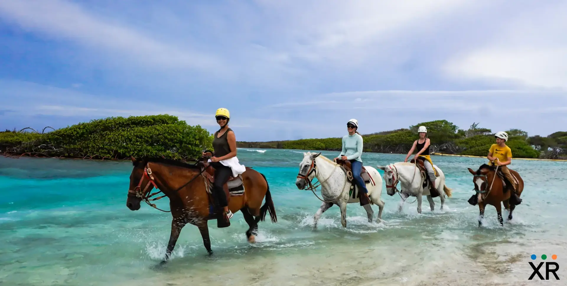 Riders on horseback in shallow turquoise water on the Xplore Roatan beach tour